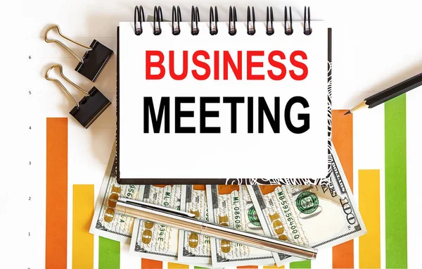 Inscription BUSINESS MEETING in the notebook, concept of planning, with office tools ,chart and dollars