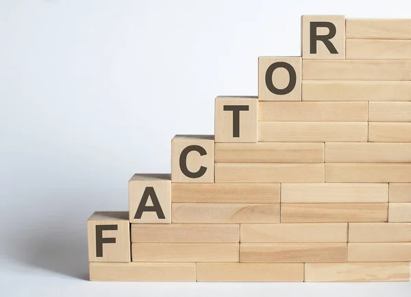 Three wooden cubes with letters FACTOR on white table.