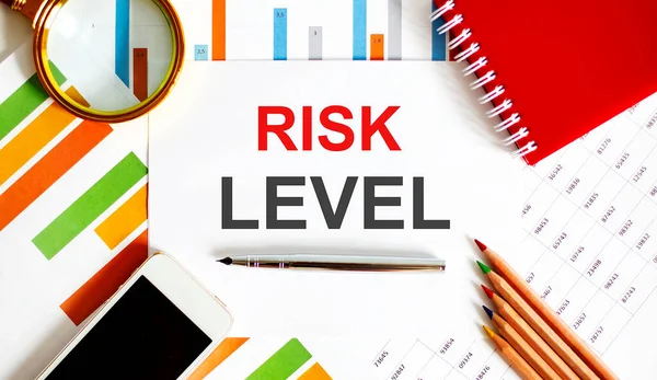Text RISK LEVEL on notepad with office tools, pen on financial report