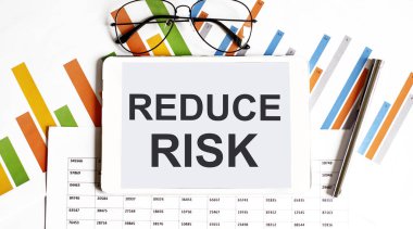 The tablet with text reduce risk. on business charts and pen