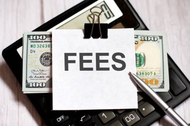 White paper with text FEES with dollars on calculator with pen