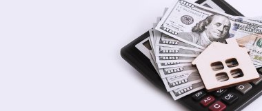 Wooden house with dollars banknotes and calculator on white background. Copy space
