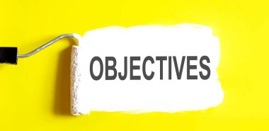 OBJECTIVES. Sarı zemin üzerinde beyaz fırça ile açık bir kutu boya. Üst görünüm.
