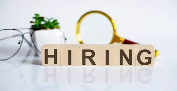 HIRING concept on wooden cubes and flower ,glasses ,coins and magnifier on the white background