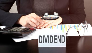 Hesap makinesi ve çizelge kullanan İş kadını ahşap masa başı ofisinde matematik finansmanı ve metin DIVIDEND ile iş geçmişi