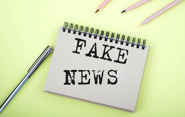 Fake News text on notebook with pen on yellow background