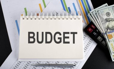 Not defterine çizelge, hesap makinesi ve dolarla yazılmış bütçe metni