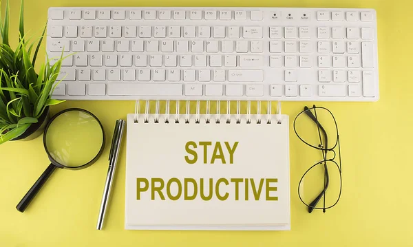 Ofis masası üst görünümü klavye ve defter metni ile sarı arkaplan üzerinde STAY Prodüktif
