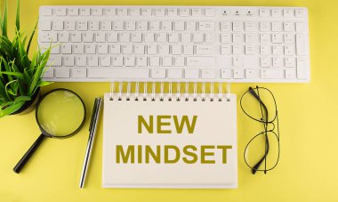 Ofis masası üst görünümü klavye ve not defteri metni ile sarı arkaplan üzerinde NEW MindSET