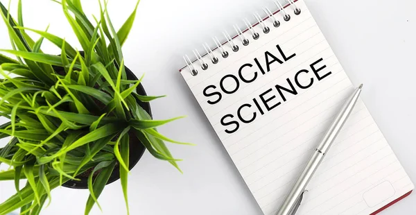 Keyword Social science - business concept text on white notebook and pen, green flowers