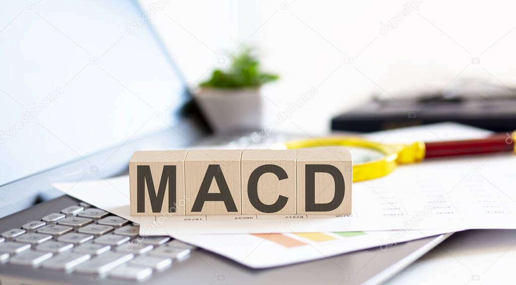 MACD - Moving Average Convergence Divergence Wooden cubes with letters on laptop keyboardwith charts , magnifier
