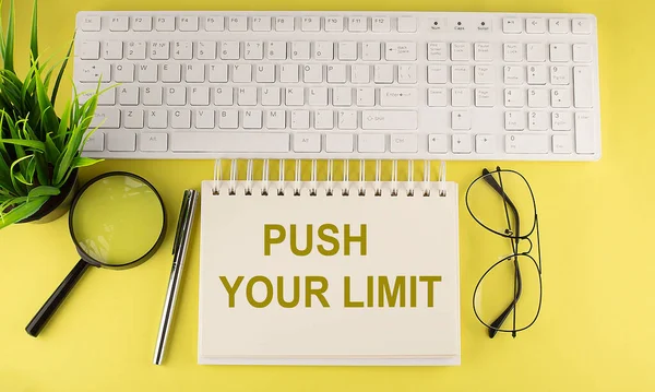 Office desk table Top view with keyboard and notebook text PUSH YOUR LIMIT on the yellow background