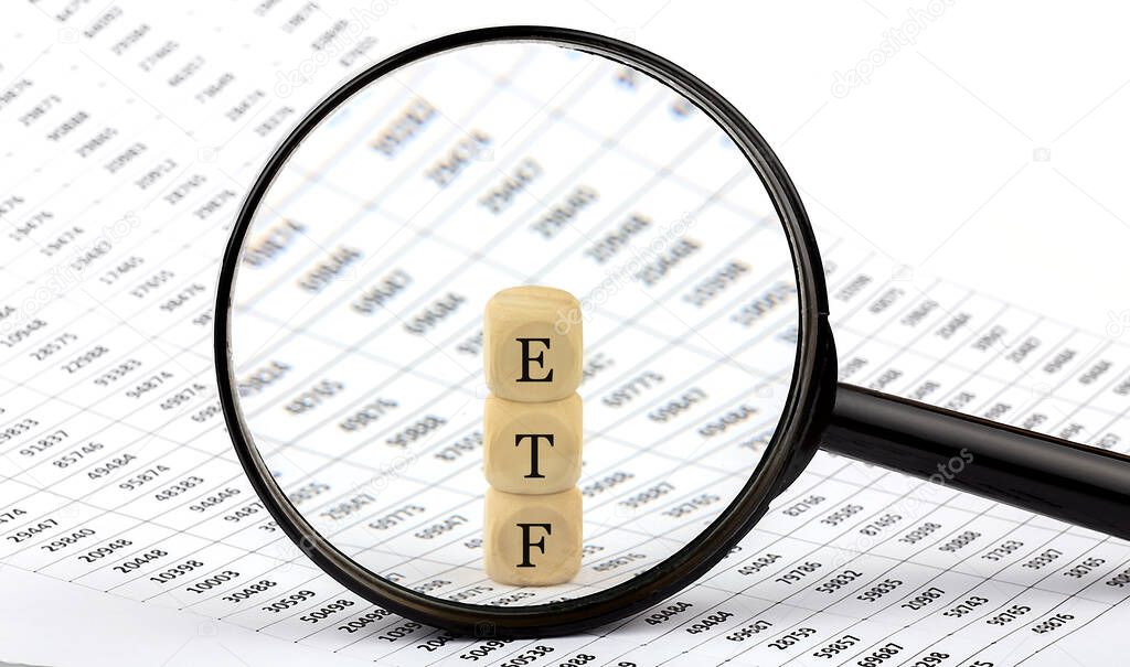 ETF wooden cubes on chart background , look through magnifier