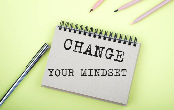 Change Your Mindset text on the notebook with pen on the yellow background
