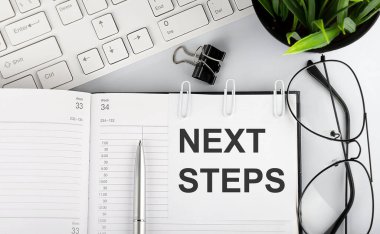 Not defterindeki beyaz etiketler üzerinde klavye ve gözlüklerle NEXT STEPS metni.