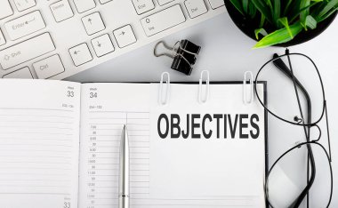 Klavye ve gözlüklü not defterindeki beyaz etiketlere OBJECTIVES metni.
