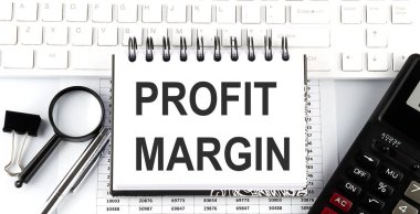 Hesap makinesi, büyüteç ve kalemle beyaz klavye üzerinde metin PROFIT MARGIN içeren beyaz defter