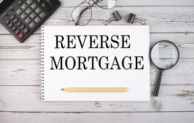 Hesap makinesi ve ofis araçları ile beyaz arkaplan üzerinde REVERSE MORTGAGE metin ile boş defter.