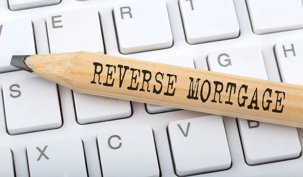 Text REVERSE MORTGAGE on wooden pencil on white keyboard. Business