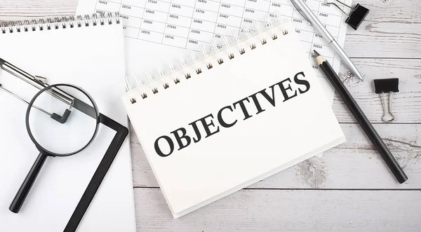 OBJECTIVES . Text written on the notepad with office tools and documents.