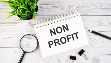NON PROFIT metin kavramı tahta arka planda ofis araçları ile deftere yaz