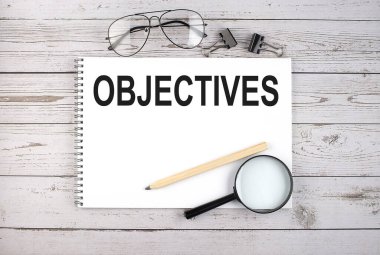 Kalem, büyüteç ve gözlük ile ahşap masa üzerinde OBJECTIVES metin defter
