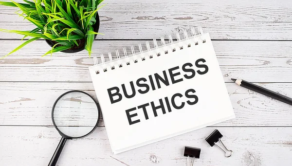 BUSINESS ETHICS text concept write on notebook with office tools on wooden background