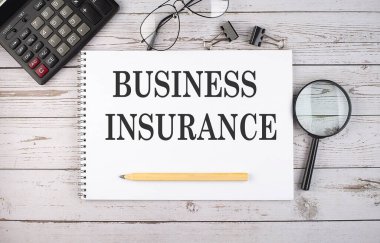 Hesap makinesi ve ofis araçları ile beyaz arkaplan üzerinde metin BUSINESS INSURANCE ile boş defter.