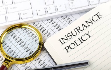 Not defterinde dosya, büyüteç, klavye ve kalemle INSURANCE POLICY metni