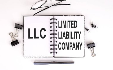 Notebook with LLC Limited Liability Company on the table with office tools clipart