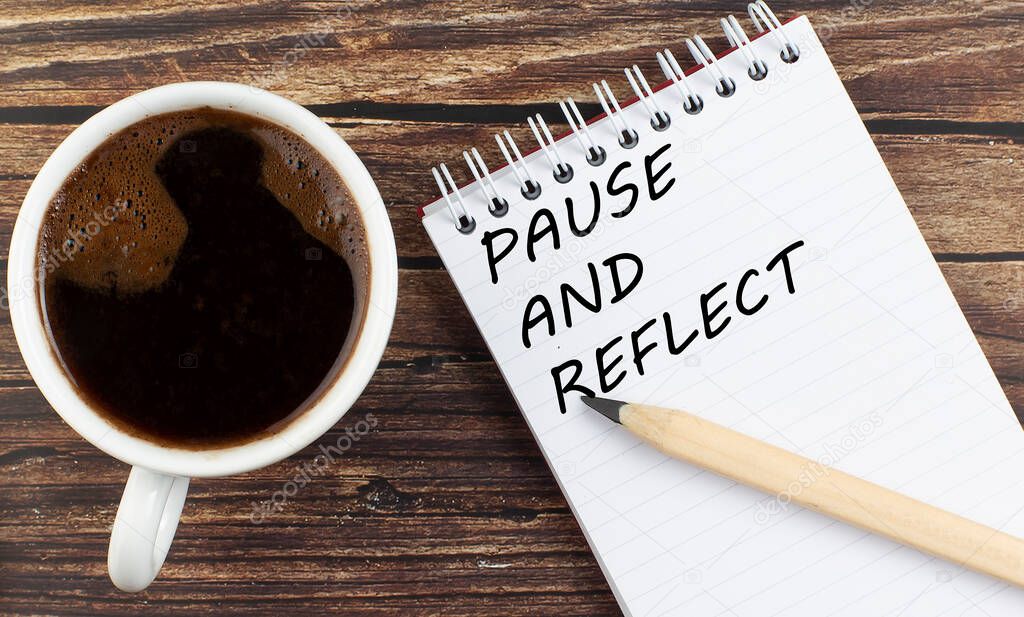 PAUSE AND REFLECT text on notebook with coffee on the wooden background