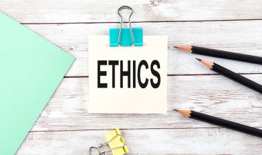 Kalemli çıkartmalar ve tahta arka planda ETHICS yazılı defter.
