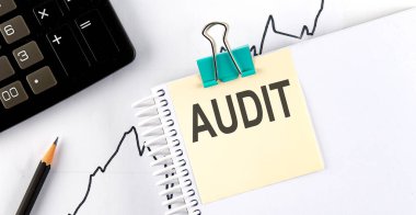 Hesap makineli bir çıkartma üzerine yazılmış AUDIT metni, grafik arkaplanındaki kalem.