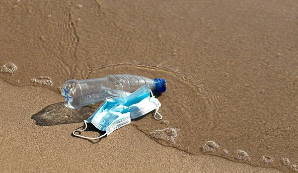 A plastic bottle lies and medical mask on the beach and pollutes the sea . The concept of pollution control the seas and oceans by plastic.