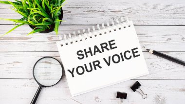 SHARE YOUR VOICE text concept write on notebook with office tools on wooden background