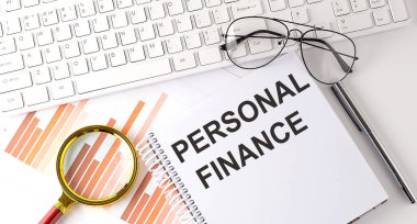 Klavye, çizelge ve gözlük ile deftere yazılmış KİŞİL FINANSA metni