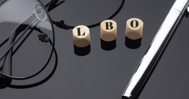 LBO concept, words on wooden blocks on black background with pen and glasses. clipart