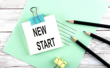 Kısa notta, tahta arka planda kalemlerle YENİ Başlat metni