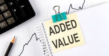 Kalemli çıkartmalar ve tahta arka planda ADDED VALUE yazılı defter.