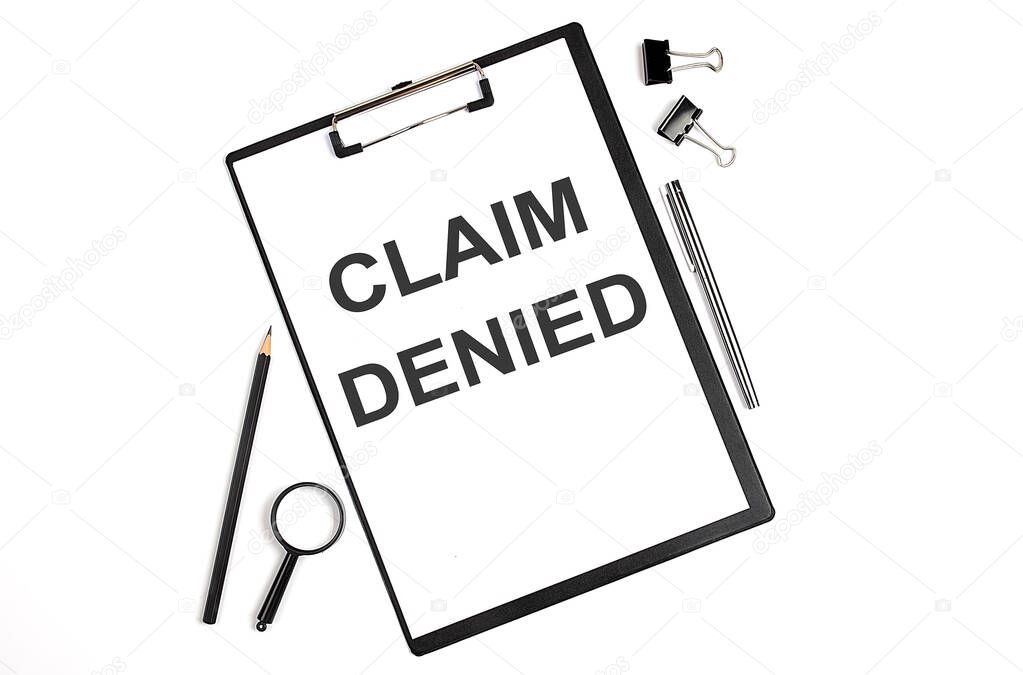 On a white background magnifier, pen and a sheet of paper with the text CLAIM DENIED. Business concept