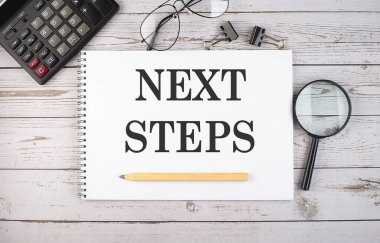 Hesap makinesi ve ofis araçları ile beyaz arkaplan üzerinde NEXT STEPS metin ile boş defter.
