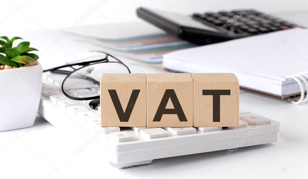 VAT written on a wooden cube on the keyboard with office tools