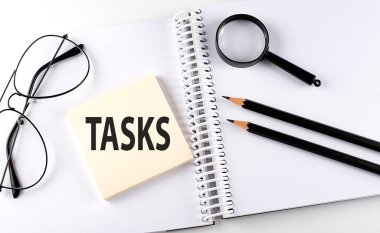 Not defterindeki hasta üzerinde kalem, büyüteç ve gözlüklü kelime TASKS