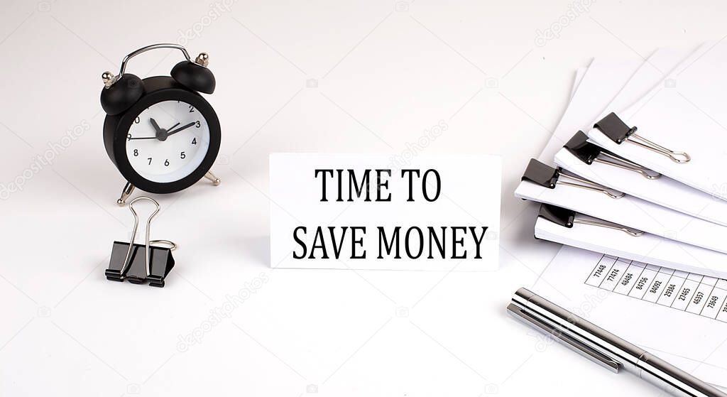 Card with text TIME TO SAVE MONEY on a white background, near office supplies and alarm clock. Business