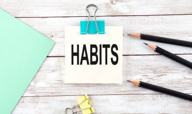 Kalemli çıkartmalar ve tahta arka planda HABITS yazılı defter.