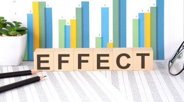Three wooden cubes with letters EFFECT on white table with keyboard and glasses