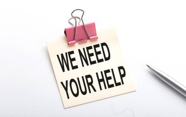 WE NEED YOUR HELP text on the sticker with pen on the white background