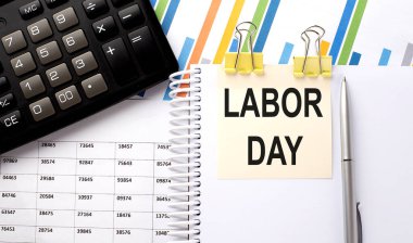 Hesap makineli bir çıkartma üzerine yazılmış LABOR Day metni, çizelge arkaplanındaki kalem.