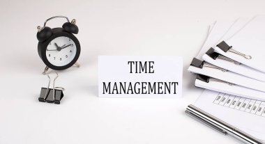 Ofis malzemeleri ve çalar saatin yanında beyaz arka planda Time ManageMENT yazılı kart. İş dünyası