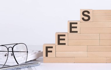 Wooden cubes with letters FEES on white table with keyboard and glasses